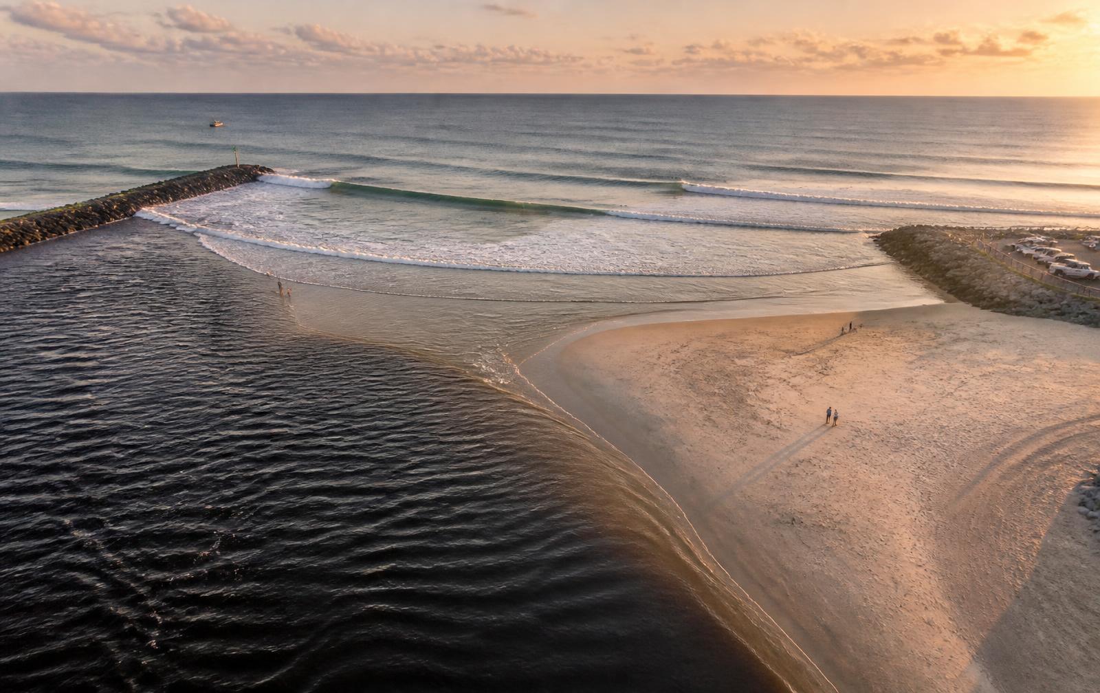 Aerial view of the New Smyrna Beach inlet with surfers and breaking waves at sunset
